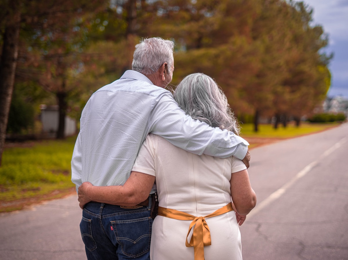 An older couple walking arm in arm along a tree-lined road